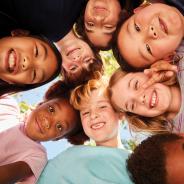 Image of a group of children in a circle looking down at central camera smiling